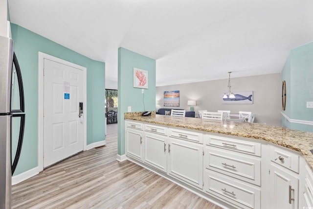 kitchen with white cabinets, hanging light fixtures, light hardwood / wood-style flooring, stainless steel refrigerator, and kitchen peninsula