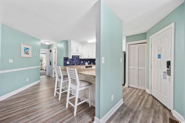 kitchen with light wood-type flooring, a kitchen breakfast bar, tasteful backsplash, and white cabinetry