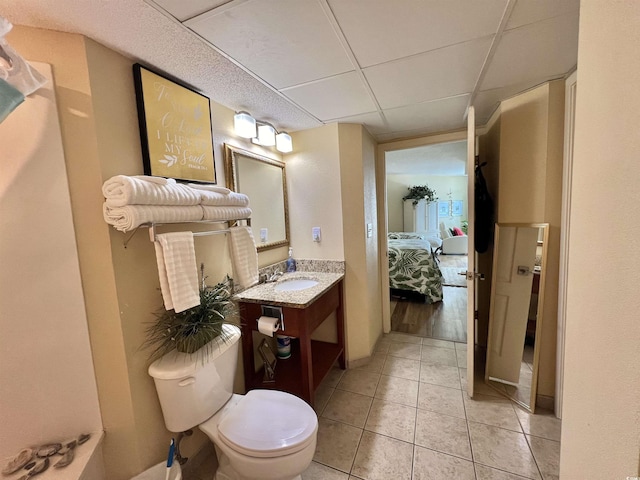 bathroom with tile patterned floors, toilet, vanity, and a drop ceiling