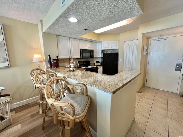 kitchen featuring black appliances, white cabinets, a kitchen breakfast bar, kitchen peninsula, and light stone countertops