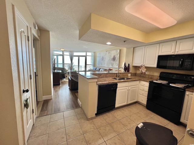 kitchen with sink, white cabinetry, light tile patterned floors, kitchen peninsula, and black appliances