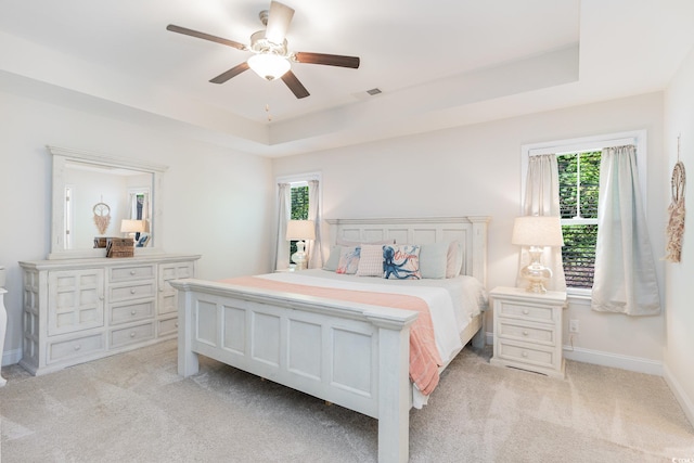 carpeted bedroom featuring a tray ceiling and ceiling fan