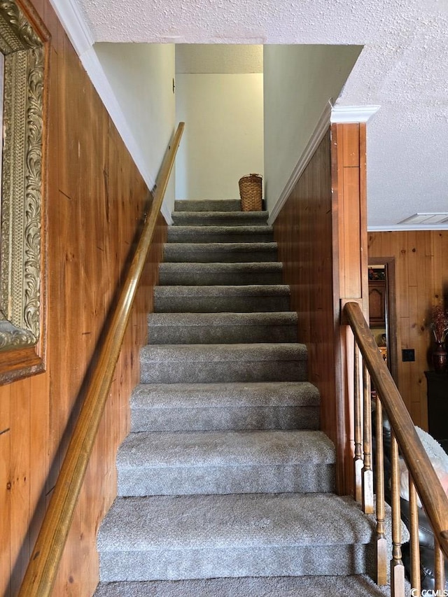 stairs featuring ornamental molding, wooden walls, a textured ceiling, and carpet floors