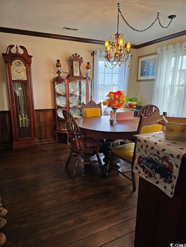 dining room featuring a textured ceiling, dark hardwood / wood-style floors, wood walls, an inviting chandelier, and ornamental molding