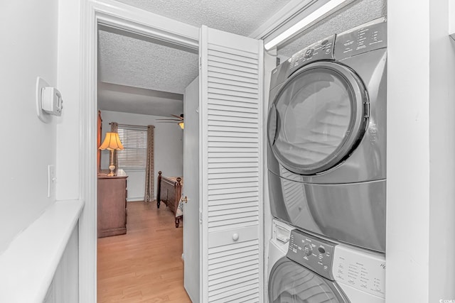 laundry room with ceiling fan, stacked washing maching and dryer, light hardwood / wood-style floors, and a textured ceiling