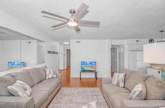 living room featuring ceiling fan, a textured ceiling, and light wood-type flooring