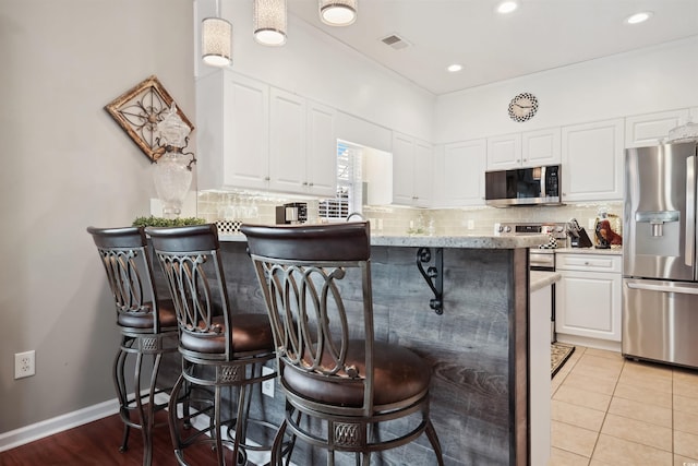 kitchen featuring stainless steel appliances, white cabinetry, a breakfast bar, and decorative backsplash