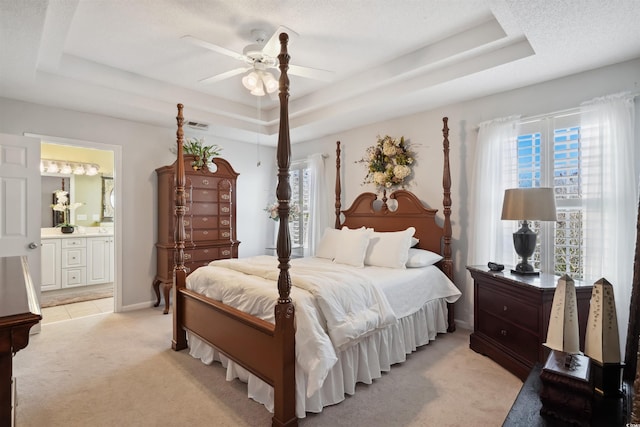 carpeted bedroom with ceiling fan, connected bathroom, a tray ceiling, and multiple windows