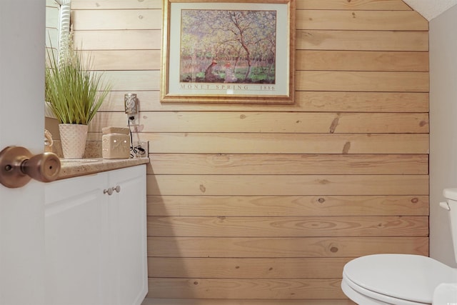 bathroom featuring vanity, wooden walls, and toilet