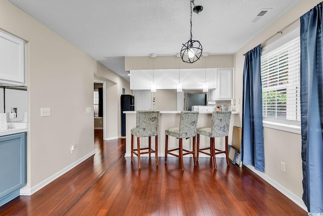 kitchen featuring a breakfast bar area, freestanding refrigerator, white cabinetry, dark wood-type flooring, and visible vents