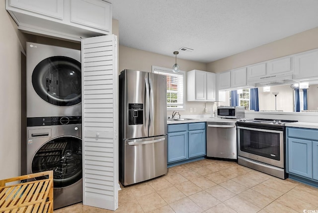 kitchen featuring stacked washing maching and dryer, light countertops, stainless steel appliances, and blue cabinetry