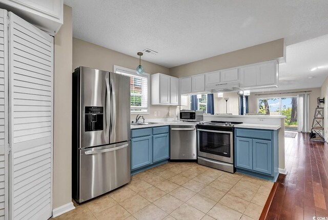 kitchen with blue cabinets, light countertops, a sink, a peninsula, and stainless steel appliances