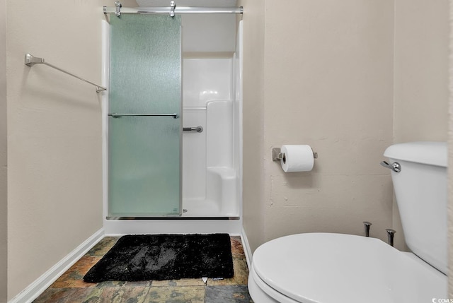 bathroom with baseboards, a stall shower, stone finish floor, and toilet