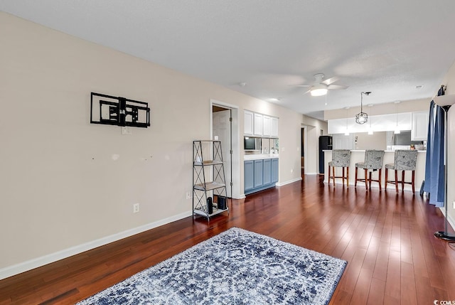 living room featuring baseboards, a ceiling fan, and dark wood-style flooring