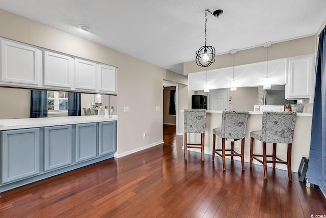 kitchen with a textured ceiling, decorative light fixtures, white cabinetry, black refrigerator, and dark hardwood / wood-style flooring