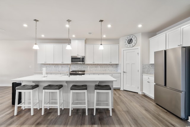 kitchen with a kitchen island with sink, light wood-type flooring, stainless steel appliances, and decorative light fixtures