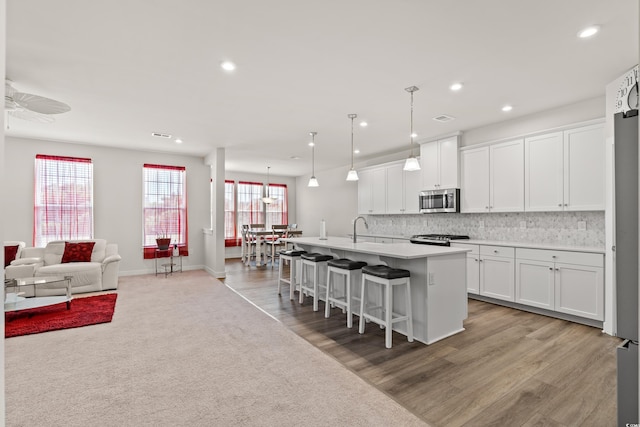 kitchen with an island with sink, light hardwood / wood-style floors, white cabinetry, and stainless steel appliances