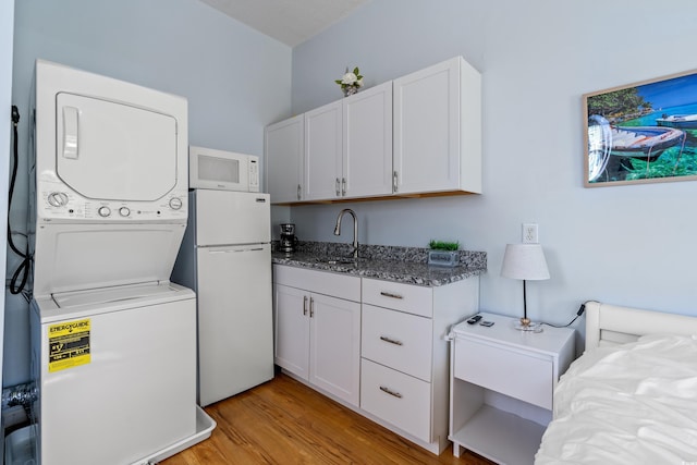 laundry area featuring stacked washer / drying machine, light wood-type flooring, and sink