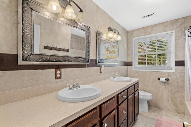 bathroom with tile patterned floors, vanity, toilet, and tile walls