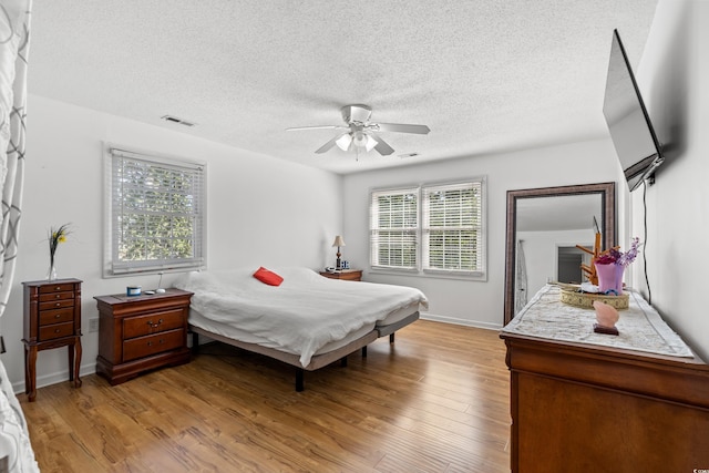 bedroom with a textured ceiling, light hardwood / wood-style flooring, and ceiling fan