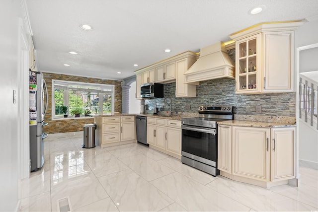 kitchen with tasteful backsplash, cream cabinets, appliances with stainless steel finishes, and custom exhaust hood