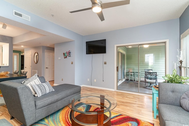 living room featuring ceiling fan, light hardwood / wood-style floors, and a textured ceiling