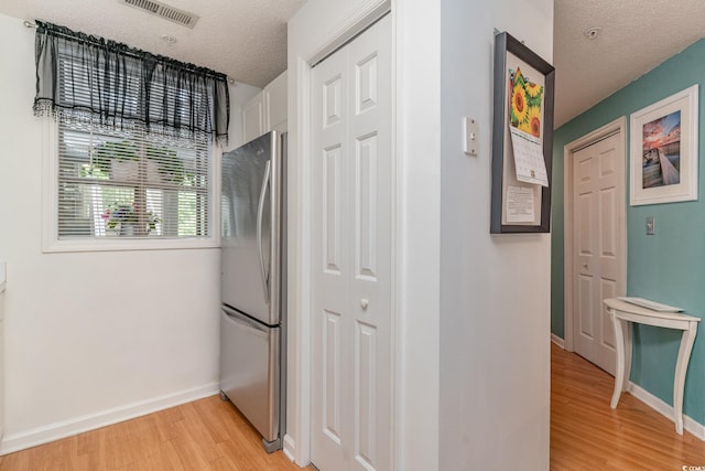 kitchen with light wood-type flooring, stainless steel fridge, white cabinetry, and a textured ceiling