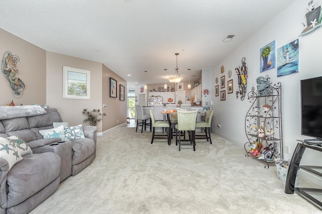 living room featuring an inviting chandelier, a textured ceiling, and light carpet