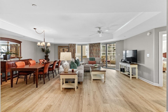 living room featuring ceiling fan with notable chandelier, a tray ceiling, light hardwood / wood-style floors, and a healthy amount of sunlight