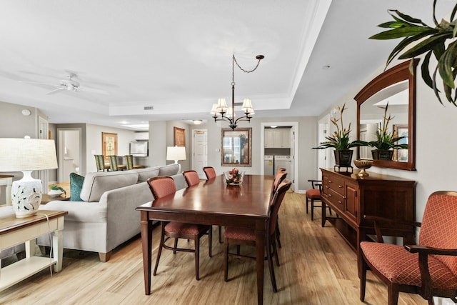 dining room with ceiling fan with notable chandelier, light hardwood / wood-style floors, a tray ceiling, and washing machine and clothes dryer