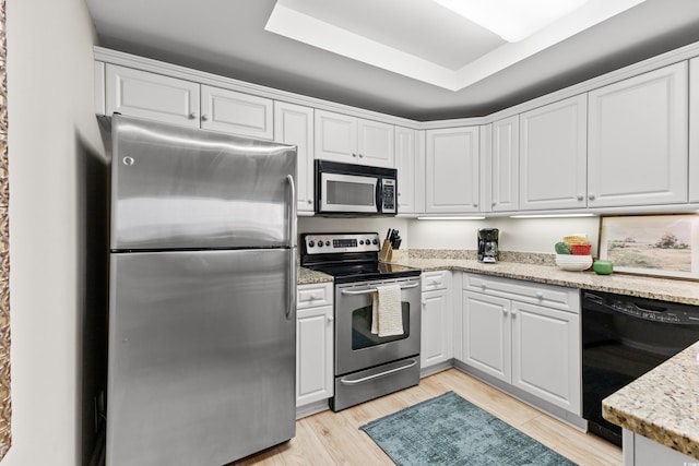 kitchen featuring appliances with stainless steel finishes, a tray ceiling, light hardwood / wood-style flooring, and white cabinets