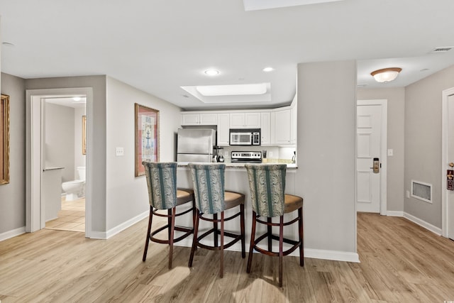 kitchen with light hardwood / wood-style flooring, stainless steel appliances, white cabinetry, and a breakfast bar area