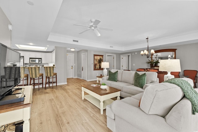 living room with ceiling fan with notable chandelier, a raised ceiling, light wood-type flooring, and ornamental molding