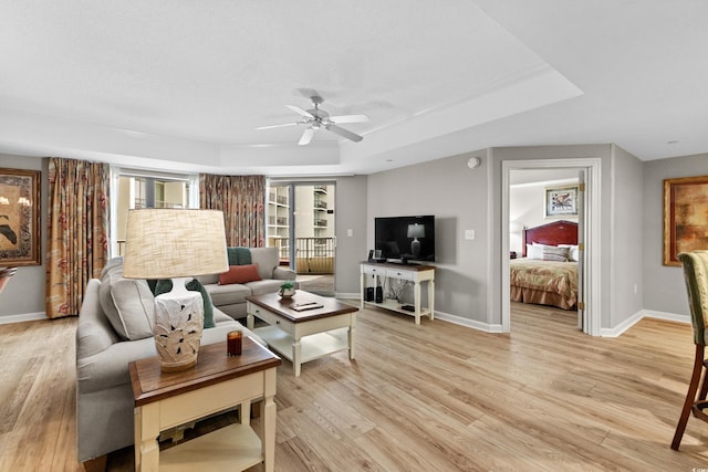 living room featuring light hardwood / wood-style flooring, ceiling fan, and a raised ceiling