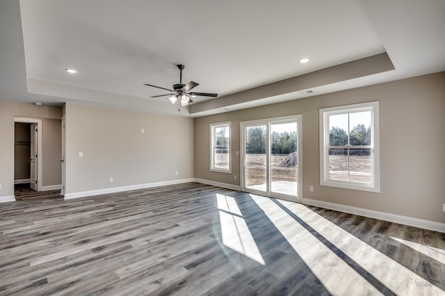 empty room with ceiling fan, a tray ceiling, and light wood-type flooring