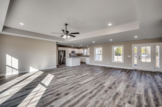 unfurnished living room with light wood-type flooring, ceiling fan, a tray ceiling, and sink