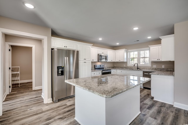 kitchen with a kitchen island, white cabinetry, stainless steel appliances, sink, and light stone counters