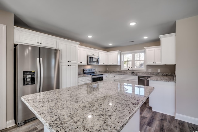 kitchen featuring white cabinets, light stone countertops, stainless steel appliances, and a kitchen island