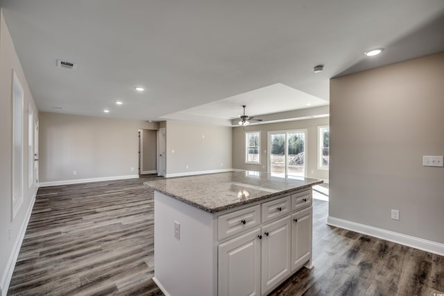 kitchen with ceiling fan, dark hardwood / wood-style floors, a kitchen island, white cabinetry, and light stone countertops