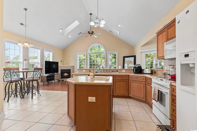 kitchen with a healthy amount of sunlight, decorative light fixtures, ceiling fan with notable chandelier, white appliances, and an island with sink