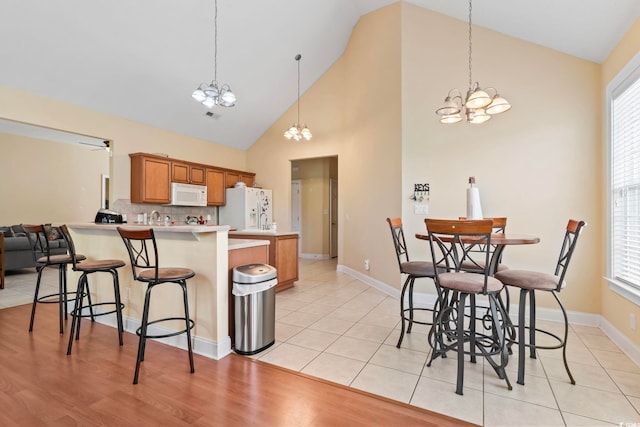 kitchen featuring hanging light fixtures, light wood-type flooring, white appliances, a chandelier, and kitchen peninsula