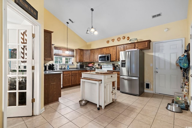 kitchen with a center island, high vaulted ceiling, stainless steel appliances, light tile patterned floors, and decorative light fixtures