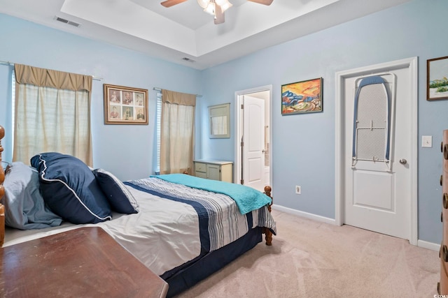 bedroom with a tray ceiling, light carpet, and ceiling fan