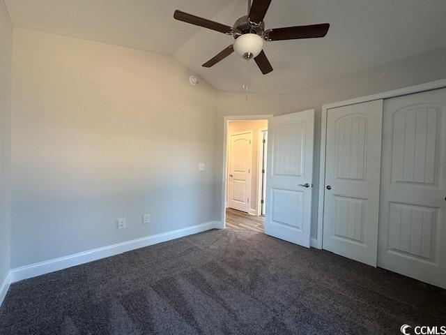 unfurnished bedroom featuring dark colored carpet, a closet, lofted ceiling, a ceiling fan, and baseboards