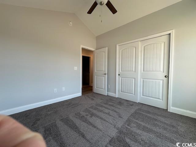 unfurnished bedroom featuring lofted ceiling, ceiling fan, baseboards, a closet, and dark colored carpet