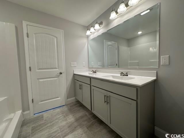 full bath featuring double vanity, a shower, a sink, and baseboards