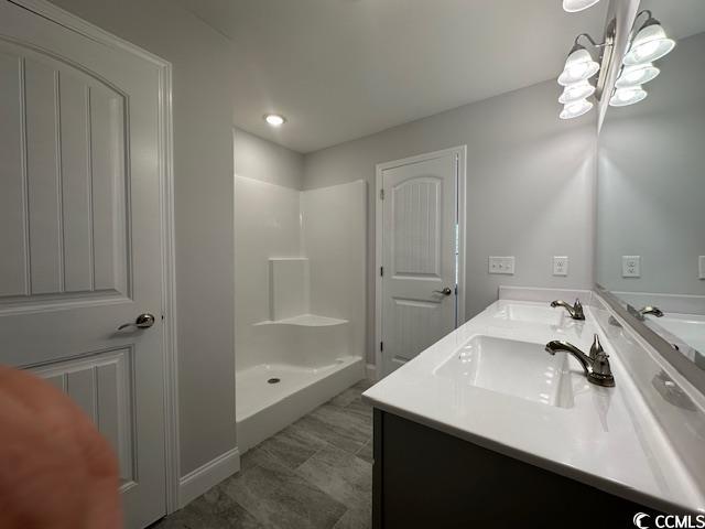 full bathroom with double vanity, a stall shower, and a sink