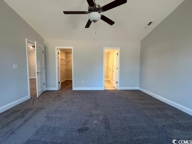 unfurnished bedroom with baseboards, a spacious closet, visible vents, and dark colored carpet