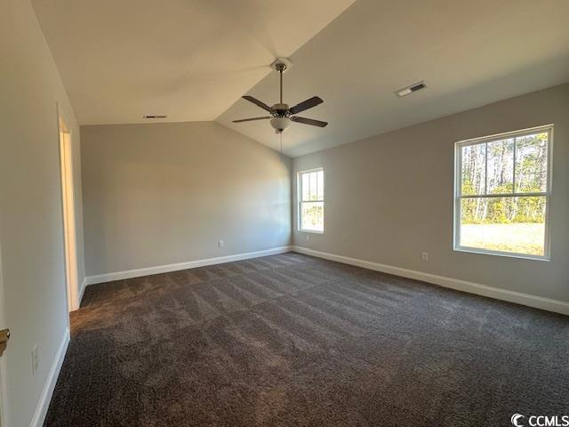 empty room featuring vaulted ceiling, dark colored carpet, visible vents, and baseboards