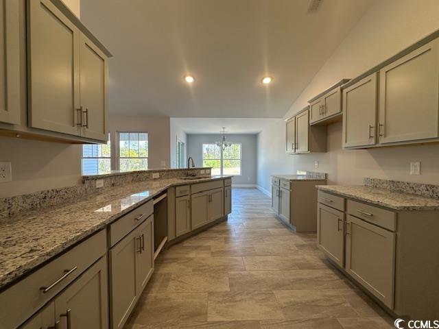 kitchen featuring lofted ceiling, dishwashing machine, light stone counters, recessed lighting, and a sink